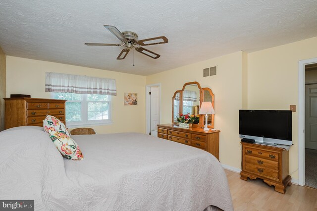 bedroom with light hardwood / wood-style flooring, ceiling fan, and a textured ceiling