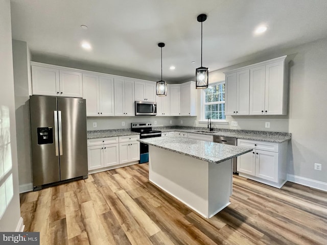 kitchen with stainless steel appliances, a center island, white cabinets, light stone countertops, and light wood-type flooring