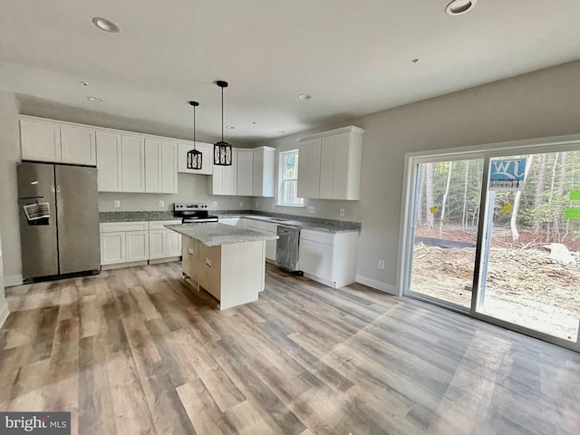 kitchen featuring stainless steel appliances, white cabinetry, light stone countertops, a center island, and pendant lighting