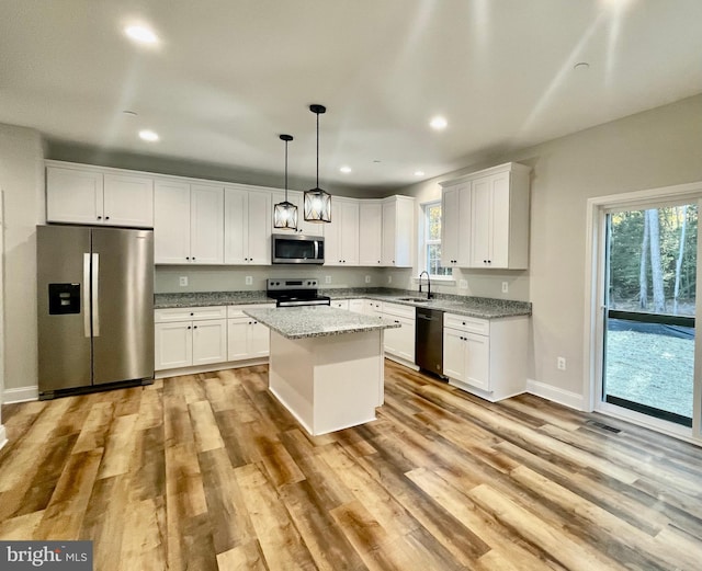 kitchen with stainless steel appliances, a kitchen island, decorative light fixtures, light hardwood / wood-style floors, and white cabinets