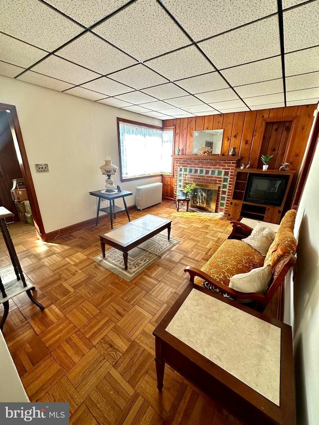 living room with a paneled ceiling, light parquet floors, radiator heating unit, and wooden walls