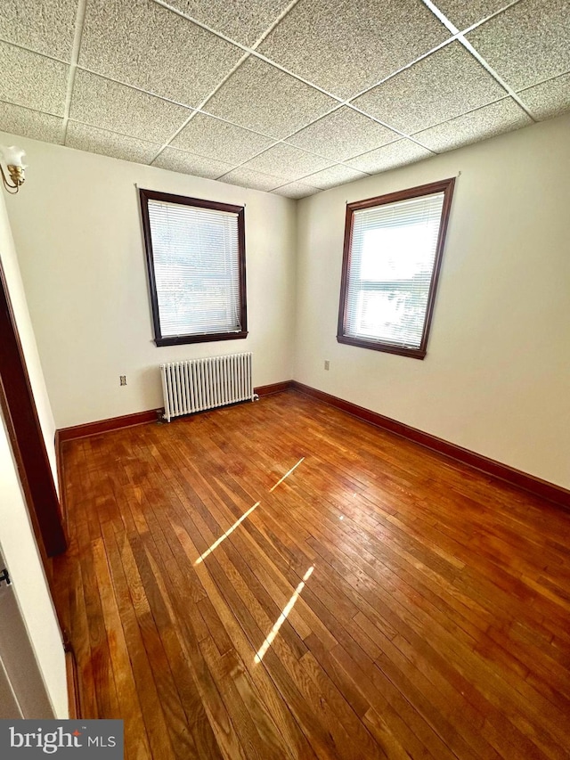 empty room featuring a drop ceiling, radiator heating unit, and hardwood / wood-style flooring