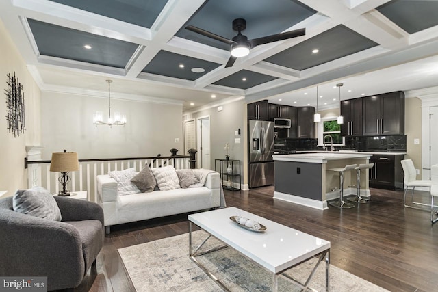 living room featuring sink, beam ceiling, dark wood-type flooring, coffered ceiling, and ceiling fan with notable chandelier