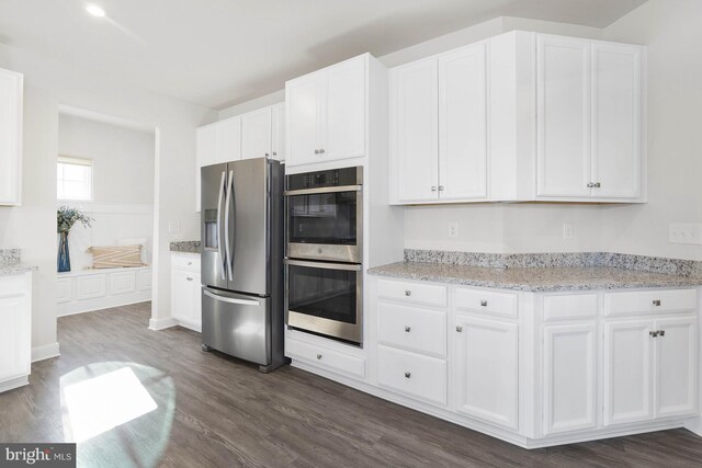 kitchen featuring appliances with stainless steel finishes, white cabinetry, dark wood-type flooring, and light stone counters