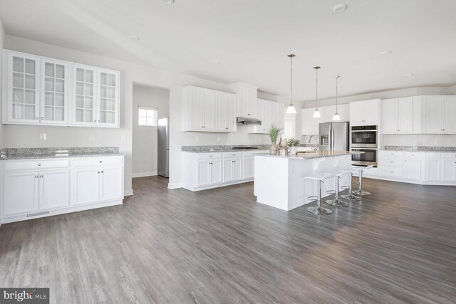 kitchen featuring pendant lighting, dark wood-type flooring, a center island with sink, white cabinetry, and stainless steel appliances