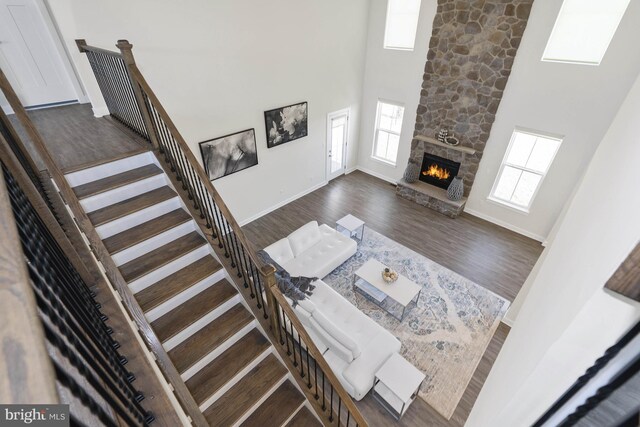 living room with a stone fireplace, dark wood-type flooring, and a high ceiling