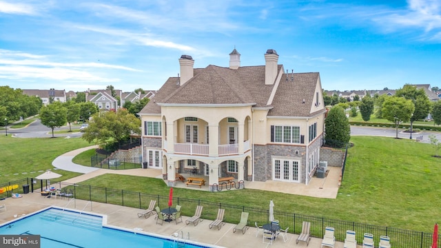 rear view of property featuring a lawn, a patio area, a balcony, and a community pool