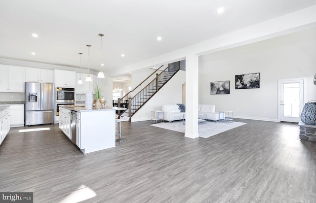 kitchen featuring a breakfast bar, a center island with sink, appliances with stainless steel finishes, decorative light fixtures, and white cabinetry