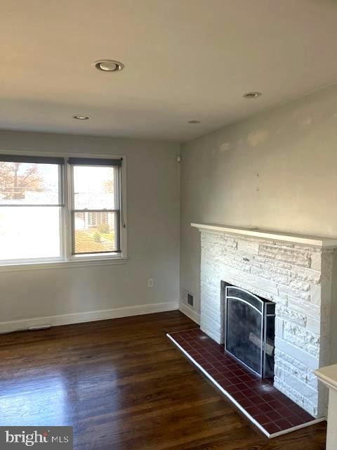 unfurnished living room featuring dark wood-type flooring and a stone fireplace