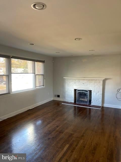 unfurnished living room featuring dark hardwood / wood-style flooring and a stone fireplace