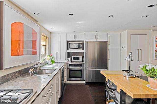 kitchen with light stone countertops, white cabinets, appliances with stainless steel finishes, and sink