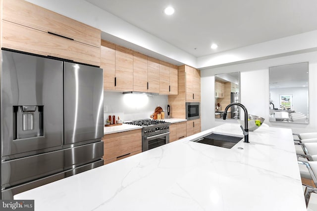 kitchen with appliances with stainless steel finishes, light stone counters, a breakfast bar area, light brown cabinets, and sink