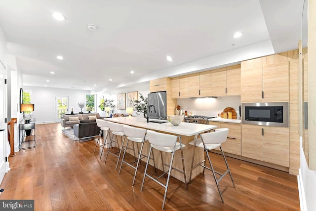 kitchen with wood-type flooring, sink, an island with sink, a kitchen bar, and stainless steel appliances