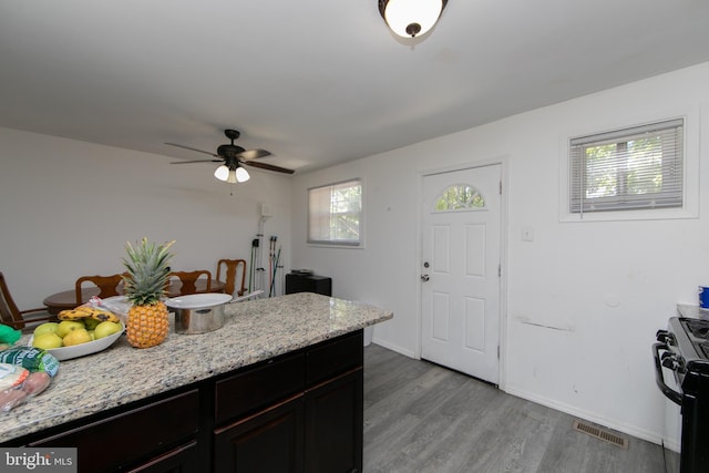 kitchen featuring light hardwood / wood-style floors, stove, ceiling fan, and light stone counters