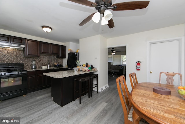 kitchen with ceiling fan, black gas range, backsplash, a breakfast bar area, and light hardwood / wood-style floors