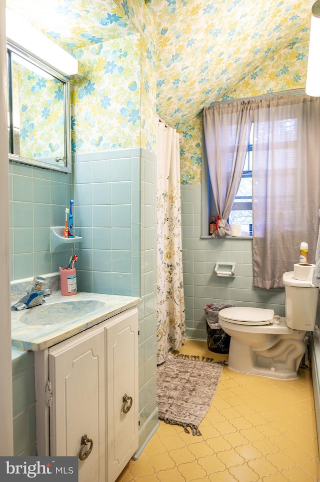 bathroom with vanity, toilet, curtained shower, tile walls, and tile patterned flooring