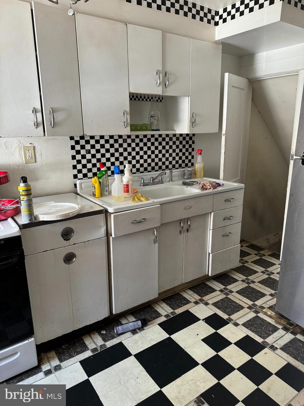 kitchen featuring white range, backsplash, sink, and white cabinetry