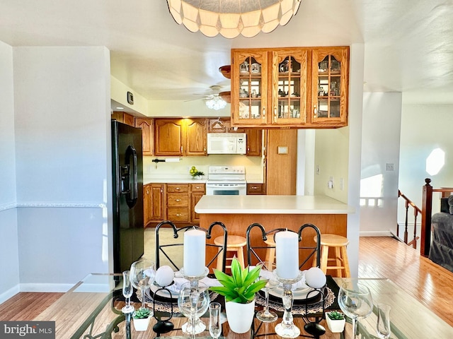 kitchen with white appliances, brown cabinetry, light wood-type flooring, a peninsula, and light countertops
