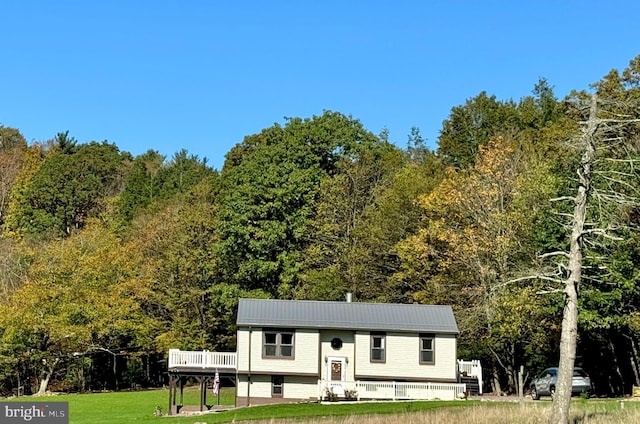 bi-level home featuring a view of trees, metal roof, and a front lawn