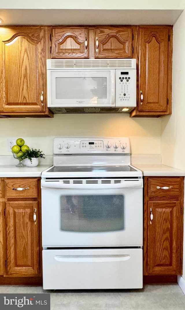 kitchen featuring brown cabinets, light countertops, and white appliances