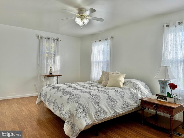 bedroom featuring baseboards, multiple windows, ceiling fan, and wood finished floors