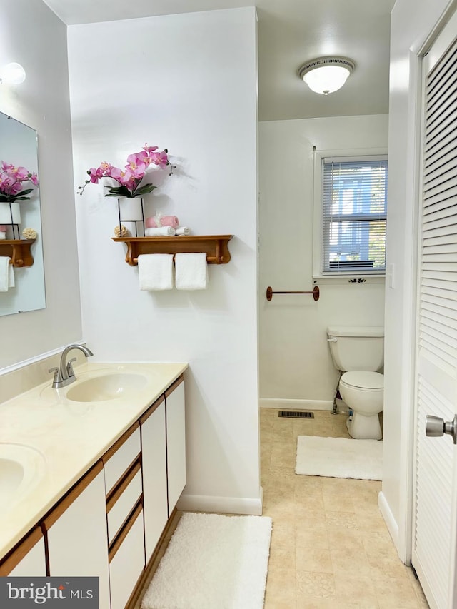 bathroom with visible vents, toilet, a sink, double vanity, and baseboards
