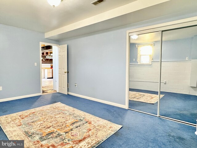 unfurnished bedroom featuring a closet, baseboards, concrete block wall, and carpet floors