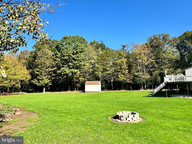 view of yard with stairway, a storage shed, a wooden deck, an outbuilding, and an outdoor fire pit