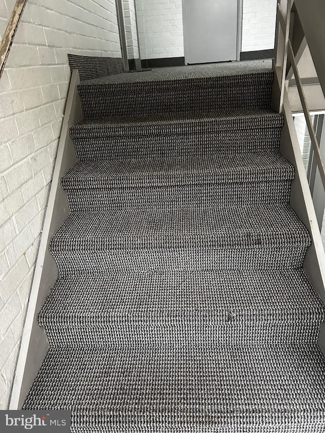 stairway featuring brick wall and carpet