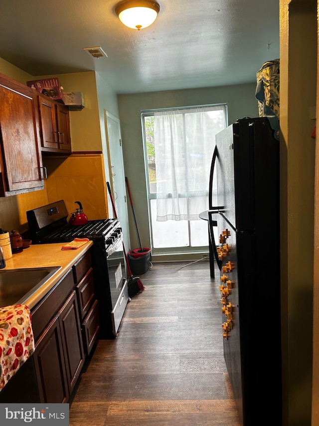 kitchen with dark wood-type flooring, black refrigerator, sink, a textured ceiling, and gas stove