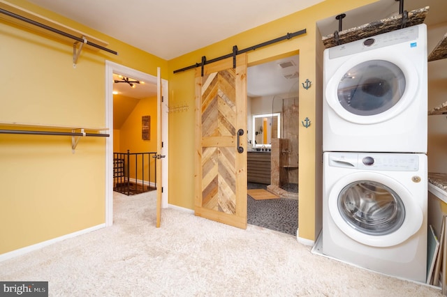 clothes washing area featuring a barn door, stacked washer and dryer, and light carpet