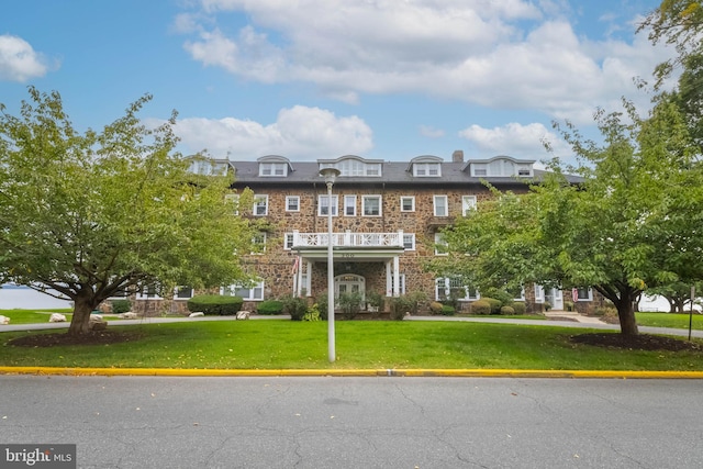 view of property featuring a balcony and a front lawn