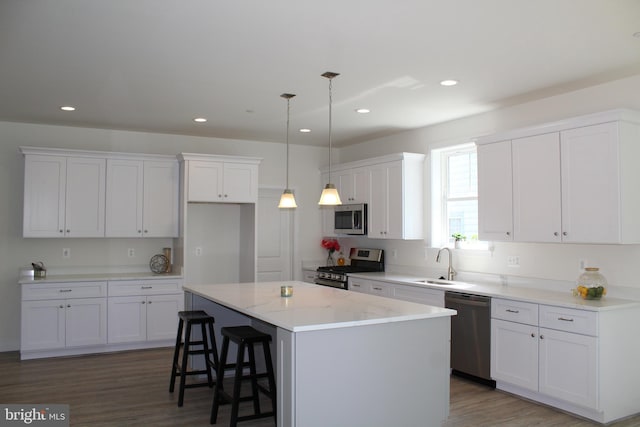 kitchen with white cabinets, a kitchen island, decorative light fixtures, appliances with stainless steel finishes, and dark hardwood / wood-style flooring