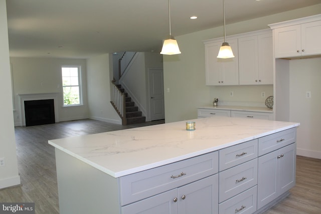 kitchen featuring light hardwood / wood-style floors, white cabinetry, light stone countertops, pendant lighting, and a center island