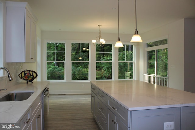 kitchen with a wealth of natural light, light stone counters, a kitchen island, and sink