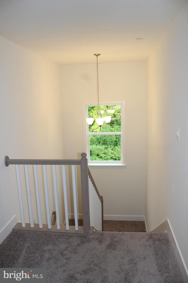 stairs with carpet floors and an inviting chandelier