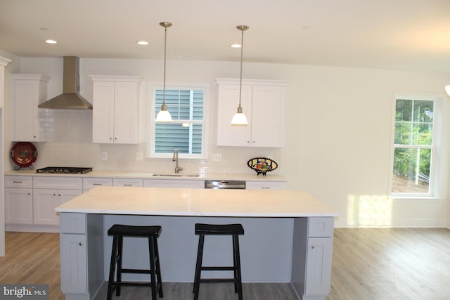 kitchen featuring wall chimney exhaust hood, a kitchen island, sink, and white cabinets