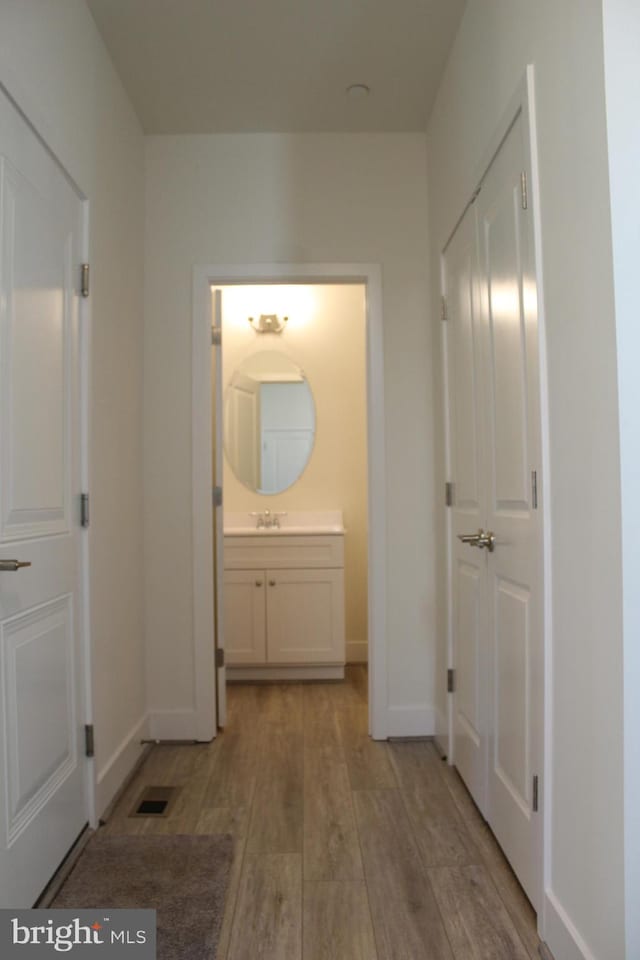 corridor with light wood-type flooring and sink