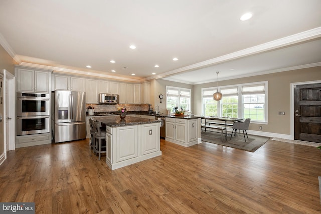 kitchen with white cabinets, hanging light fixtures, a kitchen island, wood-type flooring, and stainless steel appliances