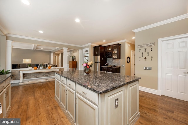 kitchen featuring wood-type flooring, cream cabinetry, ornamental molding, dark stone countertops, and ornate columns