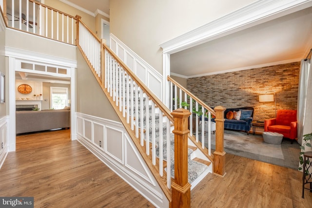 stairway with ornamental molding, wood-type flooring, a towering ceiling, and brick wall