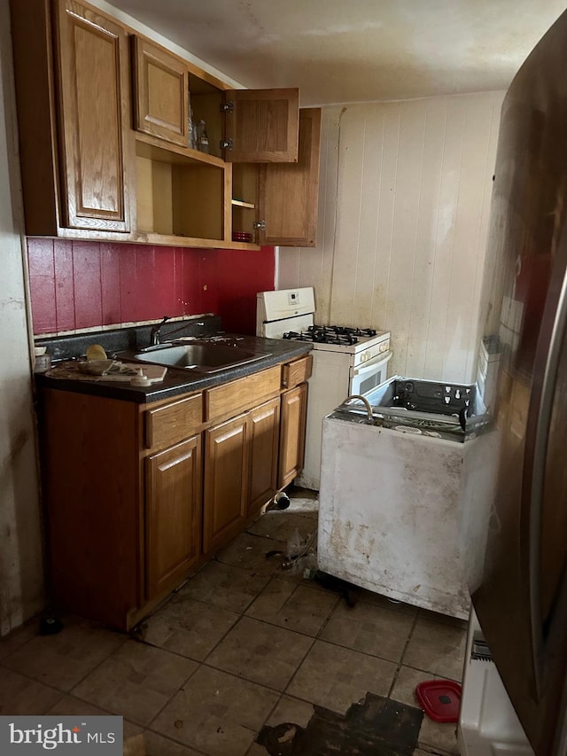 kitchen featuring wood walls, sink, white gas range, stainless steel refrigerator, and tile patterned flooring