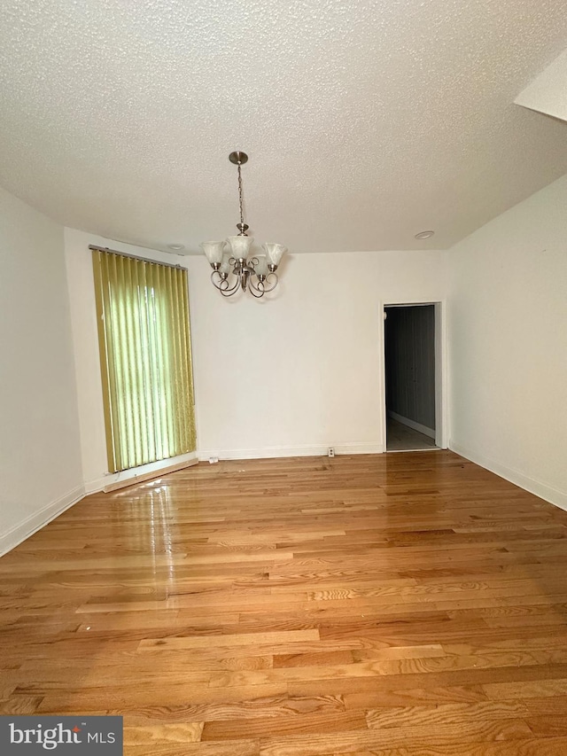 unfurnished room featuring an inviting chandelier, light hardwood / wood-style floors, and a textured ceiling