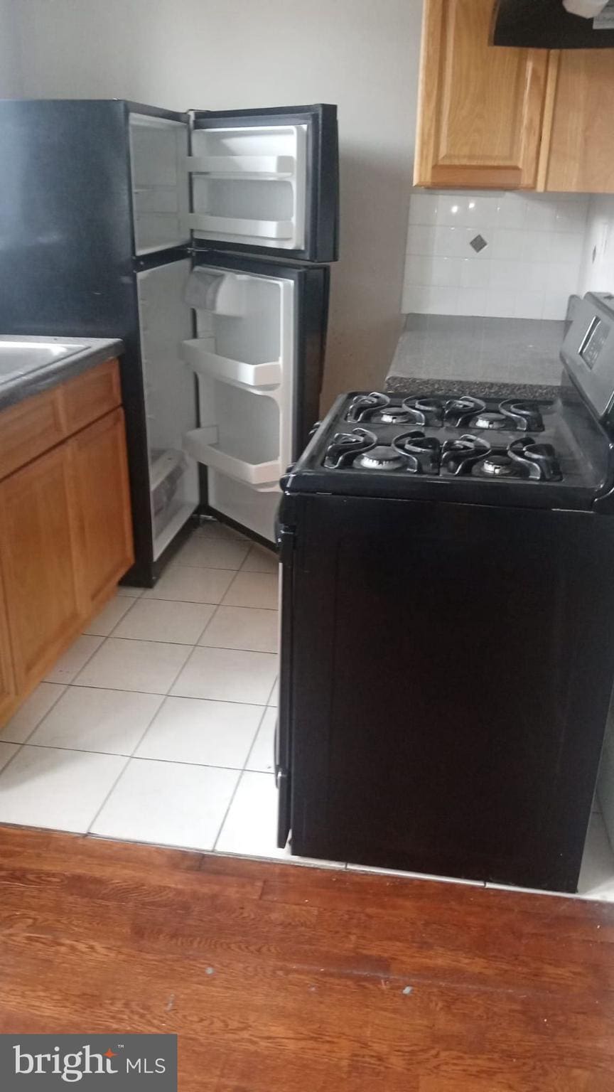 kitchen with backsplash, black range, and light tile patterned flooring