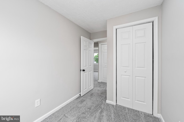 unfurnished bedroom with a textured ceiling, light colored carpet, and a closet