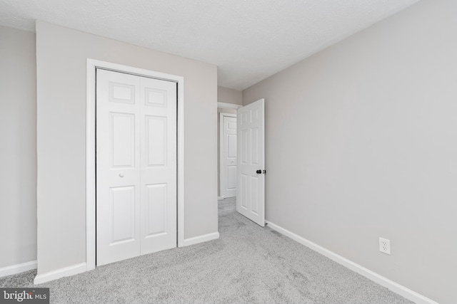 unfurnished bedroom with light carpet, a textured ceiling, and a closet