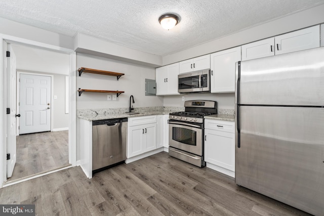 kitchen with light stone counters, white cabinets, stainless steel appliances, hardwood / wood-style flooring, and sink