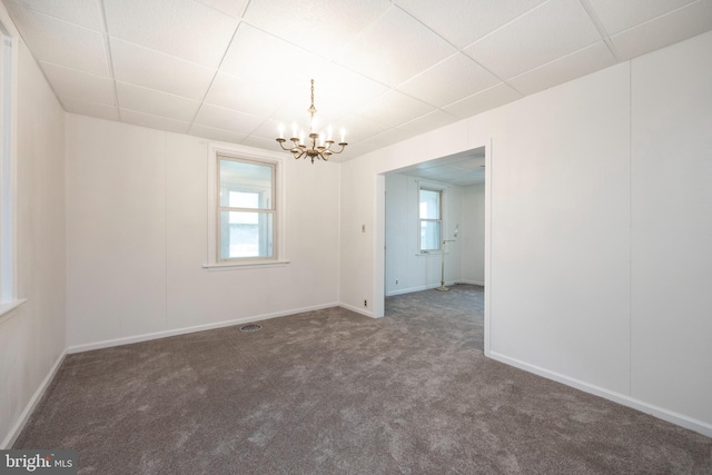 carpeted empty room with a drop ceiling and a chandelier