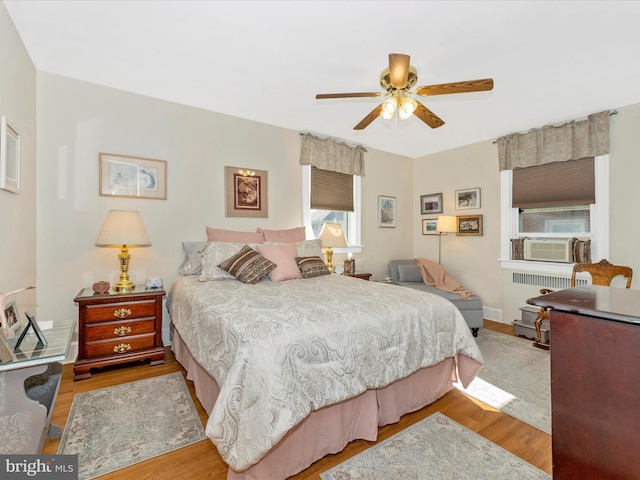 bedroom with radiator, cooling unit, light hardwood / wood-style flooring, and ceiling fan