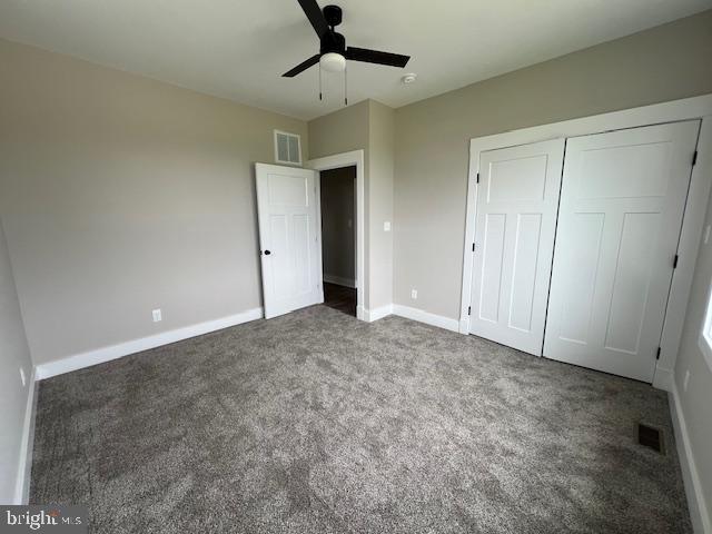 unfurnished bedroom with a closet, ceiling fan, and dark colored carpet